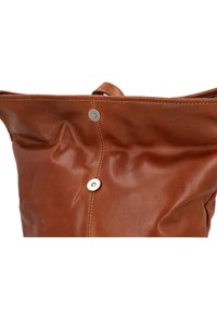 Brązowa skórzana torebka o miękkiej fakturze, zebranym wzornictwie i wyraźnym metalowym zapięciem na zatrzask. Posiada widoczne szwy wzdłuż szwów.
