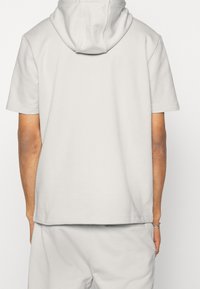 Sudadera con capucha de manga corta en gris claro y ajuste holgado. Cuenta con capucha ajustable con cordón y tejido suave y texturizado. Diseño sencillo, sin estampados ni detalles.