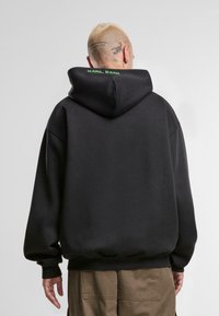 Sudadera con capucha negra de corte relajado. Cuenta con puños de canalé, una textura lisa y el logotipo verde "KARL KANI" en el cuello.