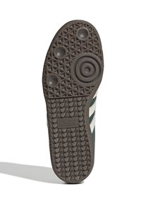 Brun gummisula på sneakers med texturerat grepp, med cirkulära mönster och en "adidas"-logotyp. Sidan har gröna och vita ränder.