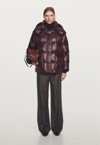Burgundy puffer jacket with a shiny texture, large hood, and two front pockets. Paired with wide-leg trousers and a brown handbag.