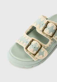 Light mint green sandal with two adjustable buckles, featuring a braided cream trim and textured sole.