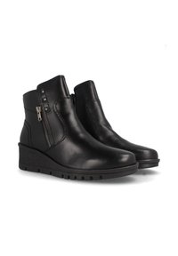Botas de tobillo de cuero negro con suela de cuña, cremalleras laterales y tachuelas decorativas. Textura suave con punta redondeada y detalles cosidos.