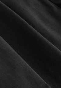 Tissu noir lisse avec une texture de tissage fin visible et des plis doux créant des ombres et des reflets diagonaux.