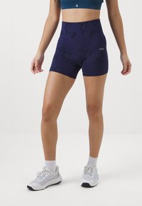 Lilla høyt belte shorts med et teksturert mønster, kombinert med en sports-bh. Modellen har på seg hvite treningstøy og ankelsokker.