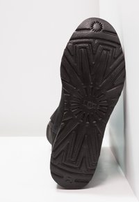 Czarna gumowa podeszwa buta z wzorem bieżnika w kształcie zygzaka, o fakturowanym wykończeniu i okrągłym logo na środku.