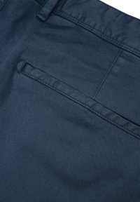 Dunkelblaues Gewebe mit glatter Textur, das mit einer Rückentasche mit angenähter Klappe versehen ist. Das Design hat ein sauberes und einfaches Finish.