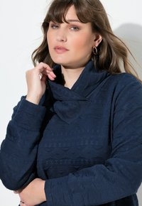 Pullover blu navy con tessuto testurizzato caratterizzato da motivi geometrici, un colletto alto e maniche lunghe.