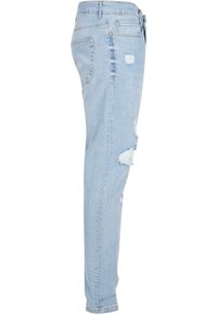 Jeans de mezclilla azul claro con corte ajustado, que presentan detalles desgastados, incluyendo desgarros en la parte frontal y un clásico diseño de 5 bolsillos.