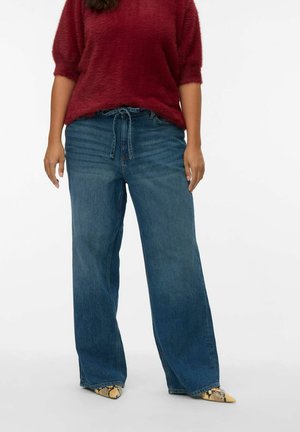 Wide-leg blue denim jeans with a high waist and drawstring detail. Paired with a fuzzy burgundy sweater and patterned pointed-toe shoes.