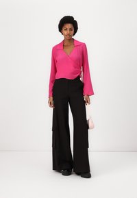 Fuchsia wrap blouse with long sleeves and a v-neckline, paired with high-waisted black wide-leg trousers and a small pink handbag.
