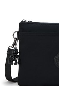 Borsa a tracolla nera in nylon con chiusura a zip, dotata di un'etichetta logo testurizzata e di un charm nero lucido attaccato. Tracolla regolabile.