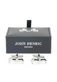 Silvriga manschettknappar formade som mustascher, visade i en svart låda med vit text, med slät, polerad metall och mjuk yta.