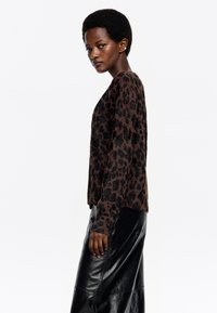 Suéter de manga larga con estampado de leopardo marrón y negro de corte relajado, combinado con una falda de cuero negro brillante. Tejido suave y texturizado.
