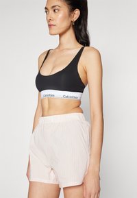 Černá sportovní podprsenka s bílým logem Calvin Klein na pružném pásku, doplněná o světle růžové pruhované šortky s elastickým pasem.