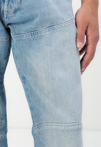 Lichtblauwe denim jeans met een rechte snit, subtiele vervaging, zichtbare stiksels en een zijzak. Geen slijtage of versieringen aanwezig.