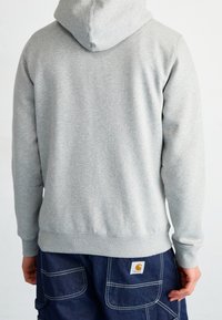 Felpa con cappuccio grigia con polsini e orlo a coste, realizzata in tessuto morbido. Abbinata a pantaloni da lavoro blu scuro con tasche laterali e patch con logo.