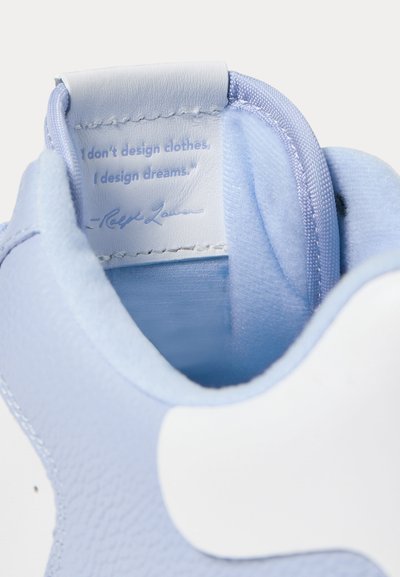 Εσωτερικό αθλητικού παπουτσιού σε ανοιχτό μπλε και λευκό με μια ραμμένη ετικέτα που γράφει, «Δεν σχεδιάζω ρούχα, σχεδιάζω όνειρα.» υπογεγραμμένο από Ralph Lauren.
