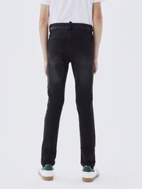 Jeans slim-fit noirs avec une taille mi-haute, poches arrière et décoloration subtile. Portés avec des baskets blanches avec des accents verts.