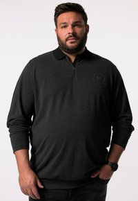Dunkelgrauer Zip-Polo-Sweatshirt mit schwarzem Kragen, langen Ärmeln und einem dezenten Logo auf der Brust. Kombiniert mit schwarzen Jeans und einer Uhr.