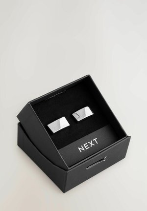 Silberne rechteckige Manschettenknöpfe, die in einer schwarzen Box mit weichem Innenfutter präsentiert werden. Sie haben eine glänzende Oberfläche und ein dezentes eingraviertes Detail.