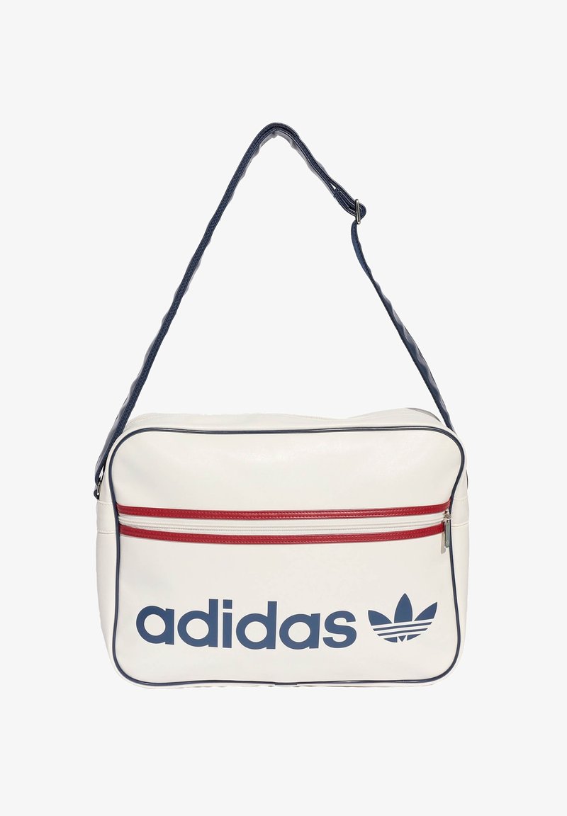 Sac à bandoulière blanc Adidas avec bordure bleu marine, poche zippée horizontale rouge, et logo ainsi que texte Adidas bleu marine à l'avant.