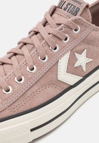 Jasnoróżowy zamszowy sneaker z białym logo w kształcie gwiazdy, okrągłym noskiem, sznurowanym fasonem, srebrnymi przelotkami oraz kontrastową czarno-białą gumową podeszwą.