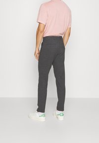 Šedé pruhované kalhoty se slim fit střihem, plochým předním dílem a zadními kapsami, které jsou v kombinaci s pastelově růžovým tričkem a bílými teniskami.