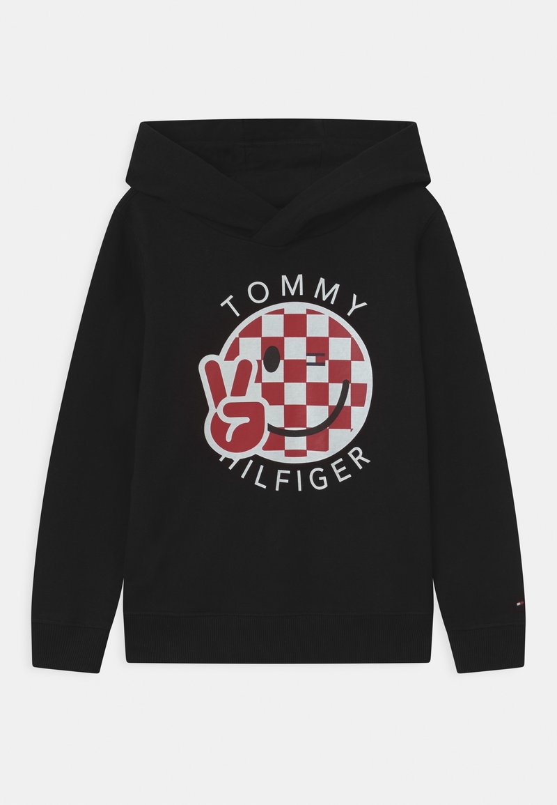 Sweat à capuche noir avec un graphique circulaire à carreaux rouges et blancs, présentant un visage souriant et un signe de paix, marqué du nom "TOMMY HILFIGER" en texte blanc.