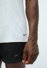 Tricou sportiv alb cu un model texturat, asociat cu pantaloni scurți negri cu o finisare texturată și logo-ul argintiu Nike pe ambele.