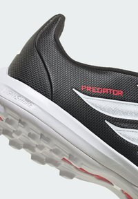 Chaussure de sport noire avec une tige texturée, des détails blancs, un logo "PREDATOR" rouge bien visible, et une semelle à motif pour une meilleure traction.