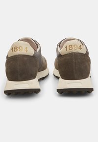 Smeđe suédne i mrežaste atletske cipele s kremastim akcentima, koje imaju broj "1894" na petama i teksturiranu gumenu đonu za prianjanje.