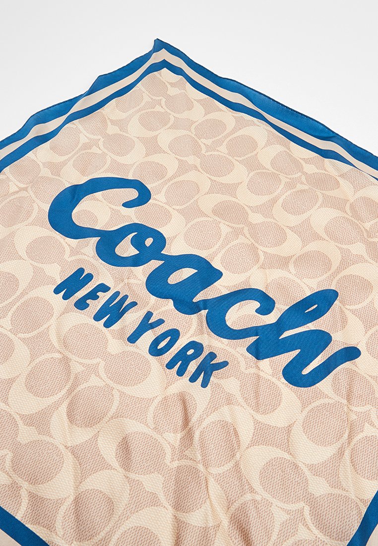 Tissu beige avec un motif texturé présentant un texte bleu "Coach New York" et une bordure bleue le long des bords.