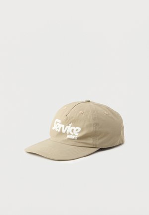 Gorra de béisbol color caqui con visera curvada, que presenta el texto en blanco "Service Works" en la parte frontal. Fabricada en tela ligera con detalles de costura.