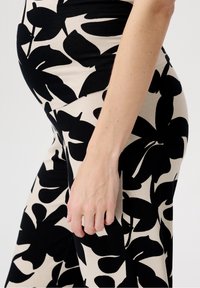 Černé a béžové šaty se vzorem s velkými květinovými motivy, vyrobené z měkké, elastické látky, které jsou přiléhavé a zdůrazňují postavu.