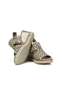 Chaussures ouvertes beige avec un design supérieur tissé, des accents métalliques et une semelle flexible de couleur claire. Présente une boucle arrière pour un enfilage facile.