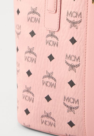 Różowa torba skórzana o fakturze, zdobiona powtarzającymi się czarnymi logo MCM oraz kształtami rombów, z detalami w postaci przeszywanych pasków.