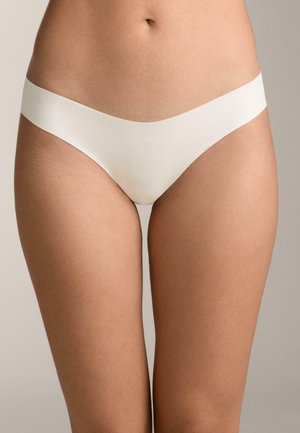 Partea inferioară a trunchiului unei persoane care poartă lenjerie fără cusături, de culoare bej deschis, pe un fundal neutru.