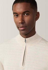 Hellbeige Zip-Kragen-Pullover aus strukturiertem Strick, mit hohem Kragen und silbernem Reißverschluss. Weiches und modernes Design.