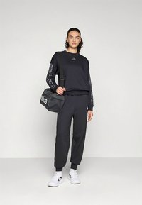 Sort atletisk genser med lange ermer, logo på brystet og mønstrede sidelister, kombinert med matchende joggebukser og hvite joggesko.