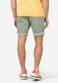 Herren Shorts mit umgeschlagenem Saum aus weichem grünen Baumwollstoff, mit entspanntem Schnitt. Kombiniert mit grauen Sneakers mit orangefarbenen Akzenten.