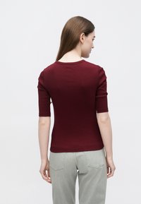 Burgunderfarget, tettsittende t-skjorte med korte ermer og rund hals, laget av glatt stoff, kombinert med lysegrå, litt vide jeans.