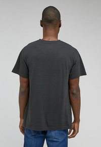 Svart bomullströja med korta ärmar, rund halsringning och avslappnad passform, bärs med blå denimjeans. Texturerad tyg med enkel design.