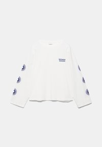 Chemise blanche à manches longues avec le texte « between seasons » sur la poitrine et des motifs de rayons de soleil bleus courant le long des deux manches.