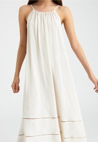 Maxikleid aus Leinen in Cremeweiß. Mit dünnen Trägern, gerafftem Halsausschnitt und horizontalen Ausschneidungen in der Nähe des Saums. Fließende Silhouette.
