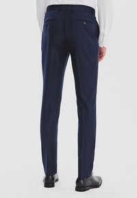 Granatowe, dopasowane spodnie o gładkiej fakturze, z dwoma tylnymi kieszeniami, w połączeniu z czarnymi eleganckimi butami.