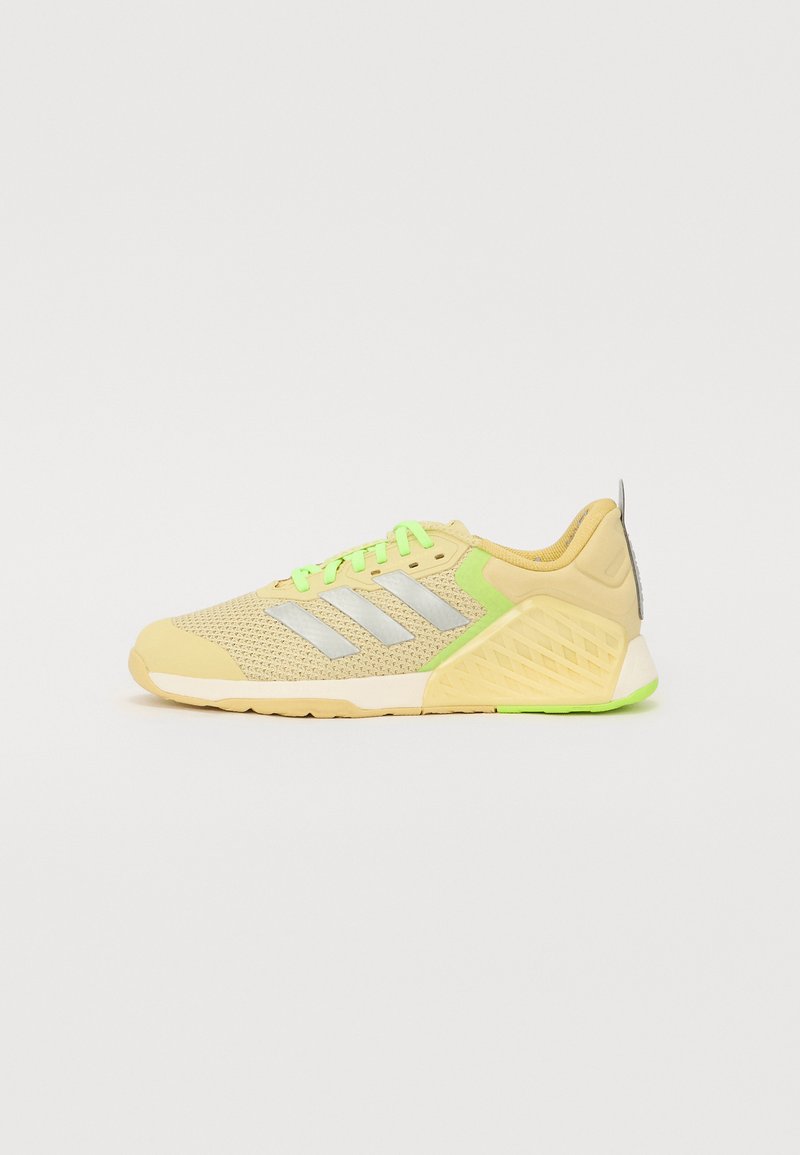 Scarpa sportiva di colore giallo chiaro con tomaia in rete, strisce grigie, lacci verde brillante e tallone testurizzato. Suola in gomma, design ammortizzato.