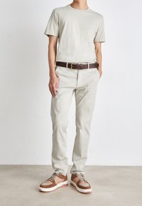 Hellgraues T-Shirt, beige Chinos und brauerlederner Gürtel. Sneaker mit einer Mischung aus hellbraun, beige und cremefarbener Farbe mit Schnürsenkeln. Sauberes Design.