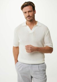 Polo bianco a maniche corte con scollo a V e motivo testurizzato, abbinato a pantaloni a righe grigio chiaro. Design casual, materiale traspirante.
