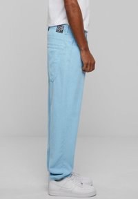 Light blue corduroy pants featuring straight legs, side pockets, and a black logo patch on the back. Paired with white sneakers.